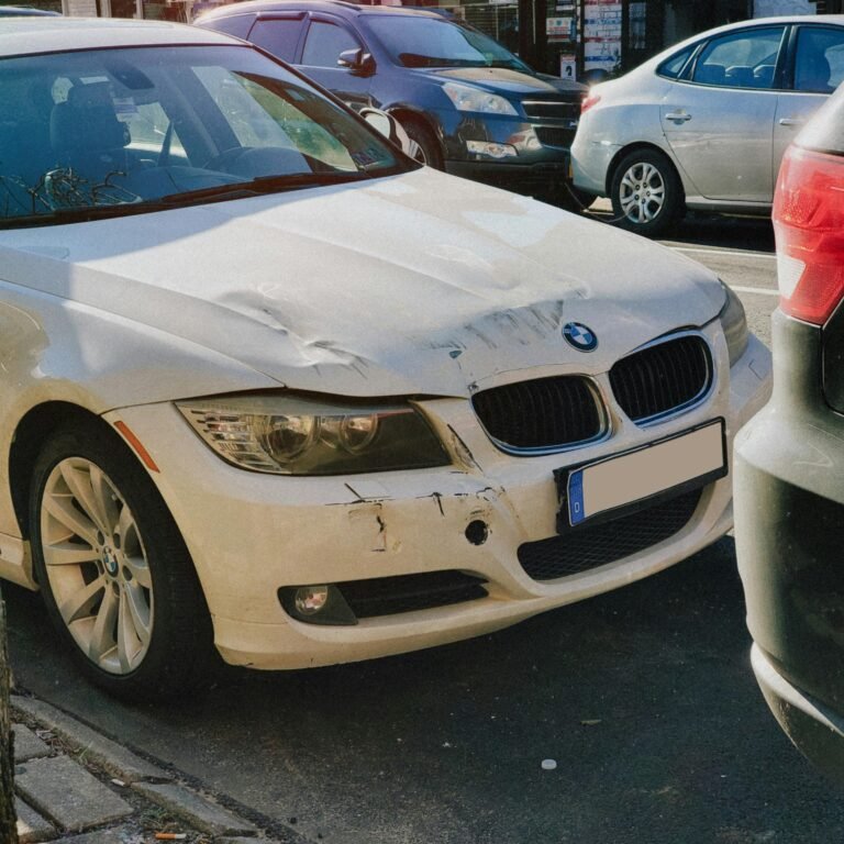White BMW sedan with front-end damage parked on a busy city street.